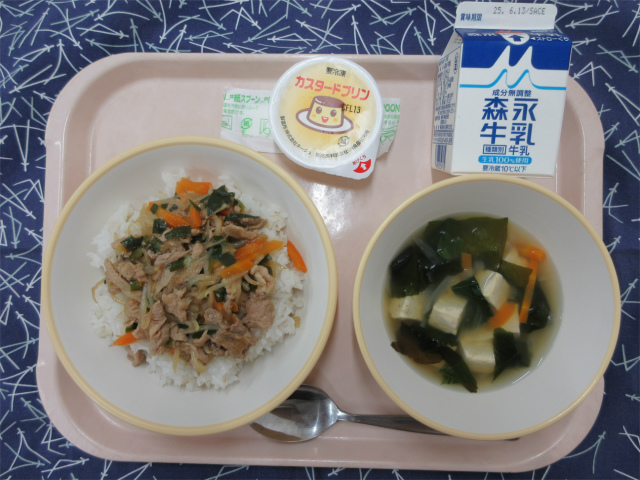 ピンクのトレーに給食が右上から反時計回りで牛乳、カスタードプリン、プルコギ丼（麦入りごはん）、豆腐スープと並べられている写真