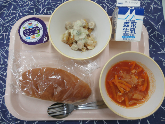 ピンクのトレーに給食が右上から反時計回りで牛乳、ポテトのチーズソース、ブルベリーゼリー、コッペパン、トマトスープと並べられている写真