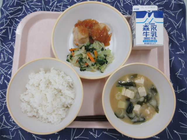 ピンクのトレーに給食が右上から反時計回りで牛乳、鶏肉の生姜焼きとじゃこサラダ、ごはん、じゃがいもの味噌汁と並べられている写真