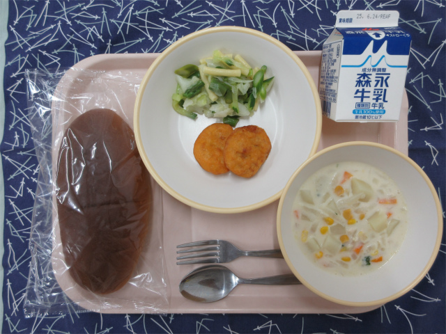 ピンクのトレーに給食が右上から反時計回りで牛乳、チキンナゲットとグリーンサラダ、黒パン、コーンのミルクスープと並べられている写真