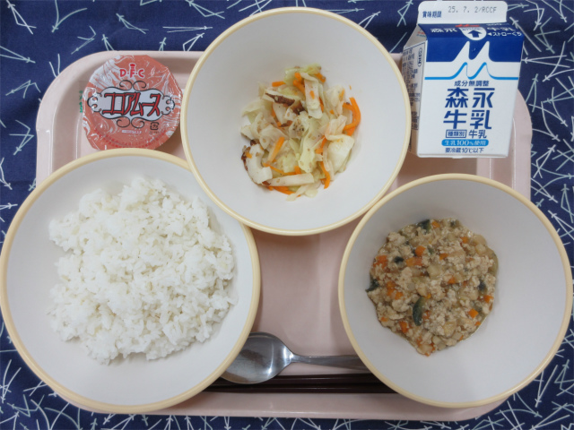 ピンクのトレーに給食が右上から反時計回りで牛乳、野菜のごま炒め、ココアムース、もち麦入りごはん、肉みそ丼の具と並べられている写真