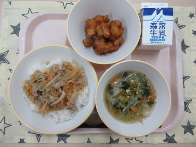 ピンクのトレーに給食が右上から反時計回りで牛乳、じゃがじゃが、チャプチェ丼（もち麦入りごはん）、五目中華スープと並べられている写真