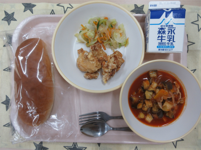 ピンクのトレーに給食が右上から反時計回りで牛乳、鶏肉のから揚げとしらたきサラダ、コッペパン、ラタトゥイユと並べられている写真