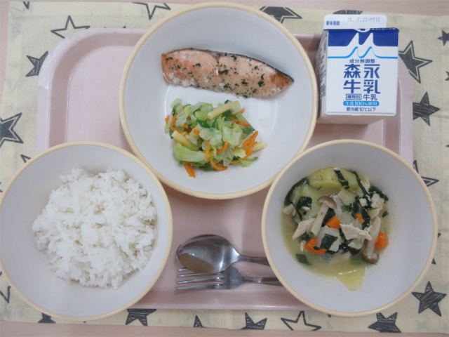 ピンクのトレーに給食が右上から反時計回りで牛乳、鮭の香草焼きとミックスサラダ、ごはん、チキンポトフと並べられている写真