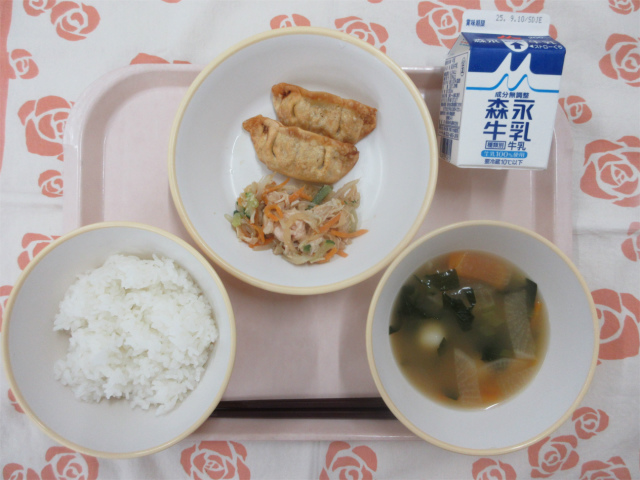 ピンクのトレーに給食が右上から反時計回りで牛乳、揚げ餃子、切干大根のサラダ、ごはん、白玉汁と並べられている写真