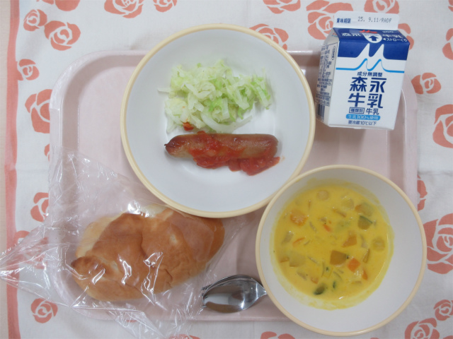 ピンクのトレーに給食が右上から反時計回りで牛乳、ゆでキャベツ、ウインナーサルサソース、サンドパン、かぼちゃシチューと並べられている写真