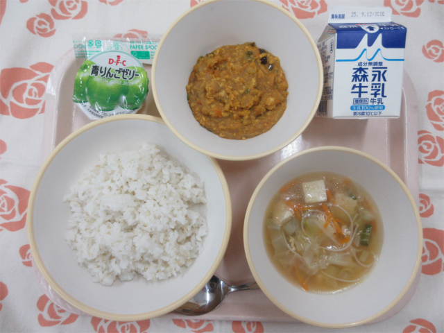 ピンクのトレーに給食が右上から反時計回りで牛乳、ドライカレー、青りんごゼリー、麦入りごはん、ビーフンスープと並べられている写真