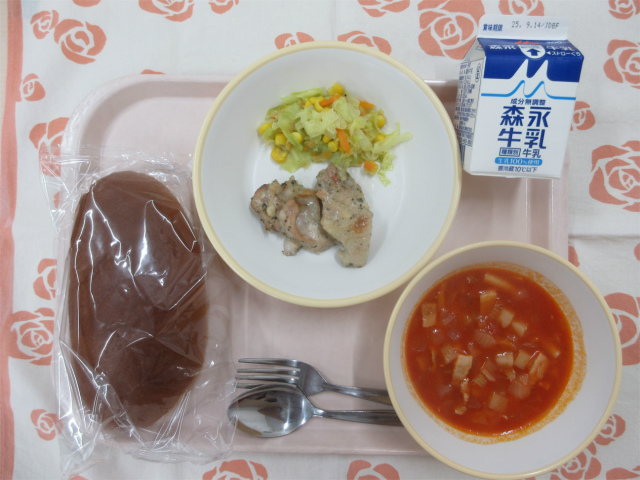 ピンクのトレーに給食が右上から反時計回りで牛乳、キャベツソテー、鶏肉のハーブ焼き、黒パン、ミネストローネと並べられている写真