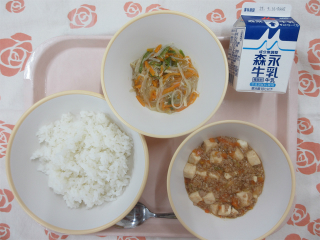 ピンクのトレーに給食が右上から反時計回りで牛乳、春雨の中華炒め、ごはん、麻婆豆腐丼の具と並べられている写真