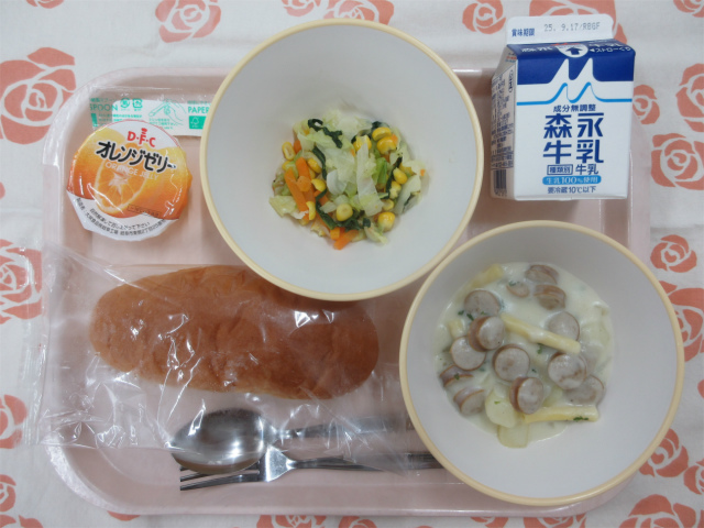 ピンクのトレーに給食が右上から反時計回りで牛乳、野菜ソテー、オレンジゼリー、コッペパン、マカロニのクリーム煮と並べられている写真