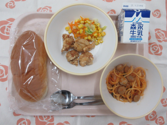 ピンクのトレーに給食が右上から反時計回りで牛乳、コーンソテー、鶏肉のから揚げ、ソフトフランスパン、なすのトマトソーススパゲッティと並べられている写真
