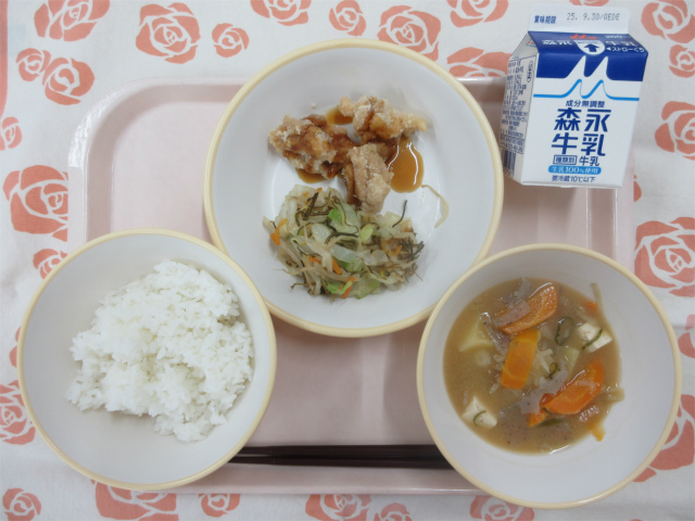 ピンクのトレーに給食が右上から反時計回りで牛乳、鶏肉の甘酢だれ、野菜の昆布和え、ごはん、みそけんちん汁と並べられている写真