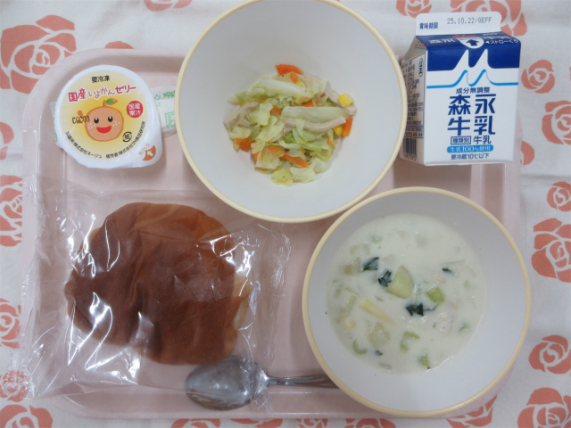 ピンクのトレーに給食が右上から反時計回りで牛乳、キャベツソテー、いよかんゼリー、米粉ロールパン、マカロニのクリーム煮と並べられている写真