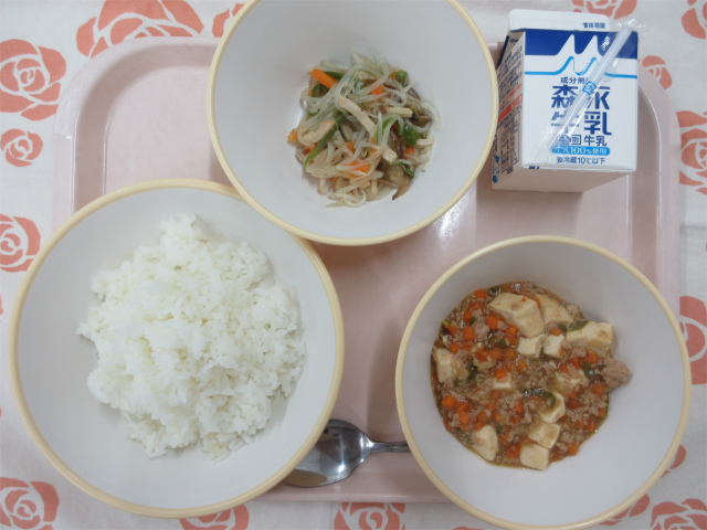 ピンクのトレーに給食が右上から反時計回りで牛乳、春雨の中華炒め、ごはん、麻婆豆腐丼の具と並べられている写真