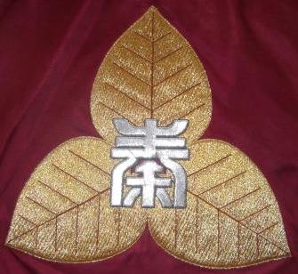 金色の三つ葉のタバコの葉の中心に、秦野市の「秦」が書かれた校章の写真