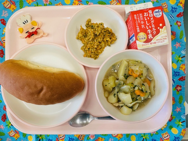 ピンクのトレーに牛乳、ドライカレー、コック帽をかぶった布製マスコット、コッペパン、やさいのスープ煮と並べられている写真