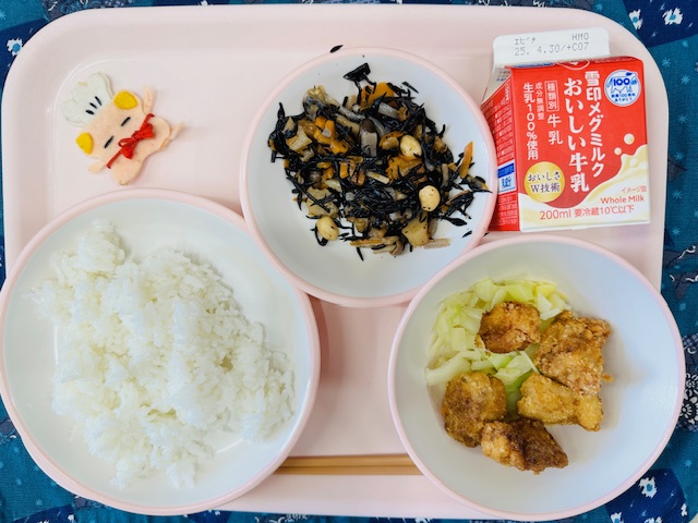 ピンクのトレーに牛乳、ひじきのいりに、コック帽をかぶった布製マスコット、ごはん、とんかつとむしキャベツと並べられている写真