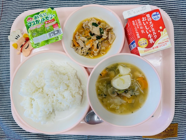 ピンクのトレーに牛乳、やきにく丼の具、マスカットゼリー、コック帽をかぶった布製マスコット、ごはん、トックスープと並べられている写真