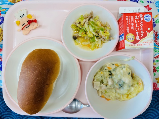 ピンクのトレーに牛乳、キャベツのサラダ、コック帽をかぶった布製マスコット、あじつきパン、ポテトグラタンと並べられている写真