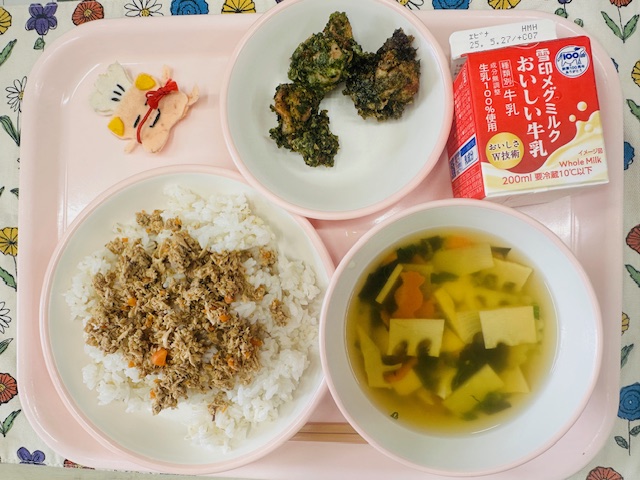 ピンクのトレーに牛乳、とりにくのころもあげ、コック帽をかぶった布製マスコット、かつおそぼろごはん、わかたけじると並べられている写真