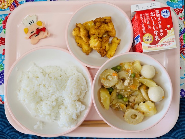 ピンクのトレーに牛乳、いかのふわっと揚げ、コック帽をかぶった布製マスコット、ごはん、じゃがいものそぼろ煮と並べられている写真