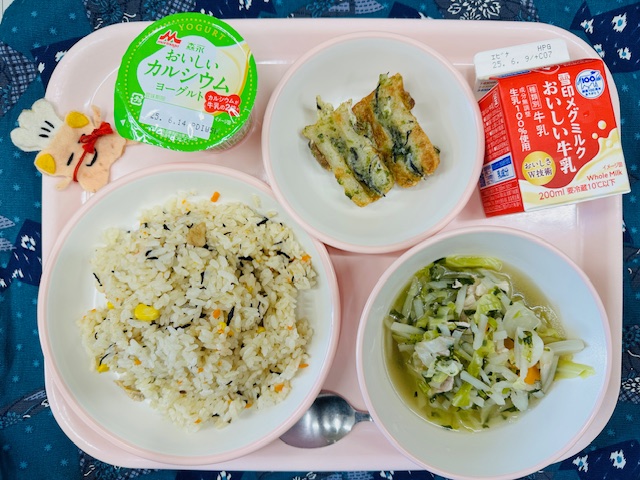 ピンクのトレーに牛乳、ちくわのいそべあげ、ヨーグルト、コック帽をかぶった布製マスコット、ひじきピラフ、やさいスープと並べられている写真