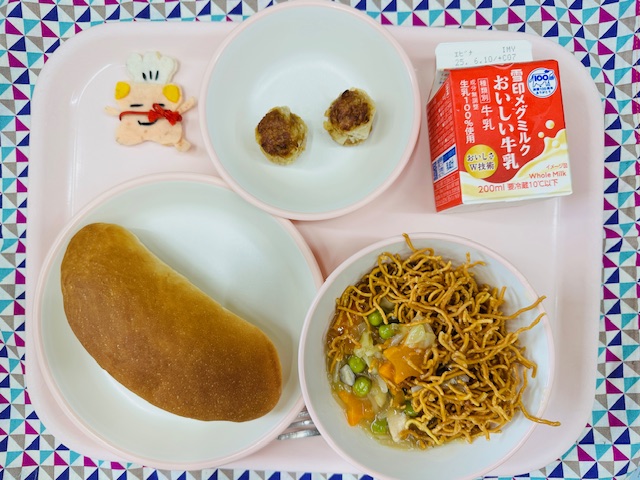 ピンクのトレーに牛乳、あげしゅうまい、コック帽をかぶった布製マスコット、コッペパン、やきそばあんかけと並べられている写真