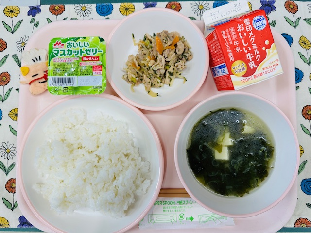 ピンクのトレーに牛乳、野菜入り焼肉、マスカットゼリー、コック帽をかぶった布製マスコット、ごはん、韓国風わかめスープと並べられている写真