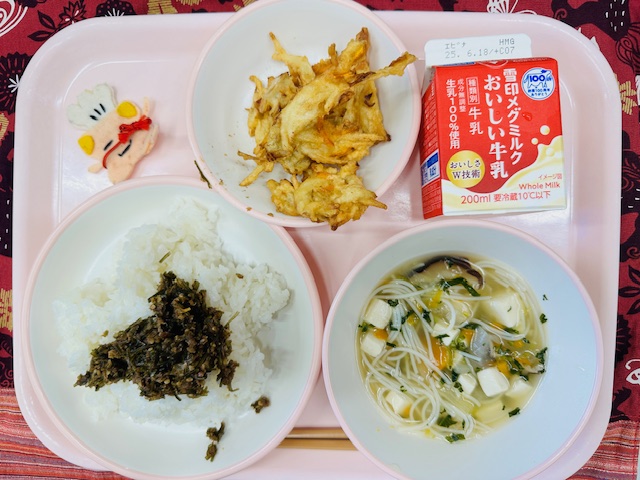 ピンクのトレーに牛乳、かきあげ、コック帽をかぶった布製マスコット、ごはんとうめこんぶ、ビーフンスープと並べられている写真