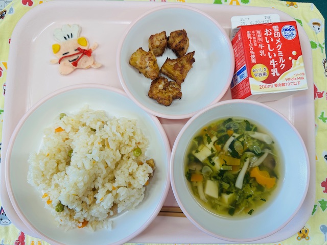 ピンクのトレーに牛乳、ぶたにくのかおりあげ、コック帽をかぶった布製マスコット、かしわずし、すまし汁と並べられている写真