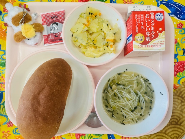 ピンクのトレーに牛乳、じゃがいものチーズ焼き、チョコだいずペースト、犬のような布製マスコット、コッペパン、ビーフンスープと並べられている写真