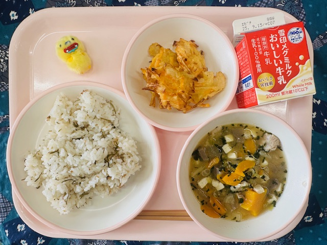 ピンクのトレーに牛乳、いかとやさいのかきあげ、黄色の布製マスコット、うめごはん、あっさりとんじると並べられている写真