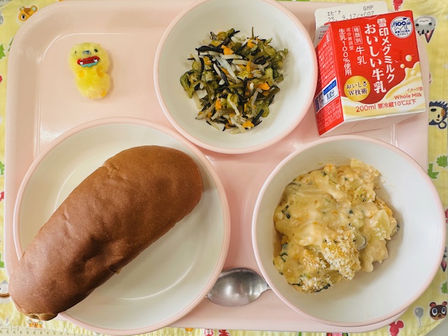 ピンクのトレーに牛乳、かいそうサラダ、黄色布製マスコット、くろパン、ポテトグラタンと並べられている写真