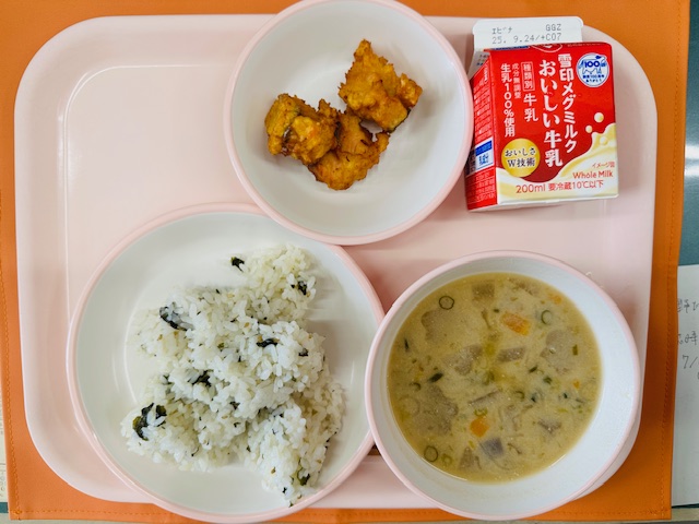 ピンクのトレーに牛乳、鮭のころもあげ、わかめごはん、ごじると並べられている写真