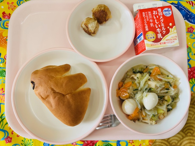 ピンクのトレーに牛乳、ごもくやきそば、あじつきパン、あげしゅうまいと並べられている写真