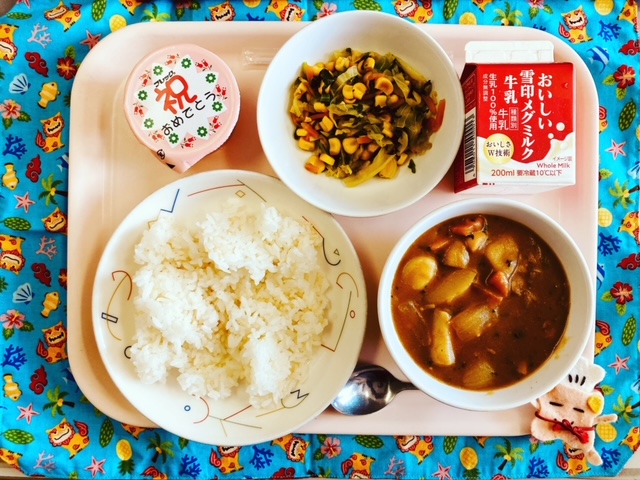 ピンクのトレーに給食が右上から反時計回りで牛乳、野菜ソテー、デザート、ごはん、チキンカレーと並べられている写真