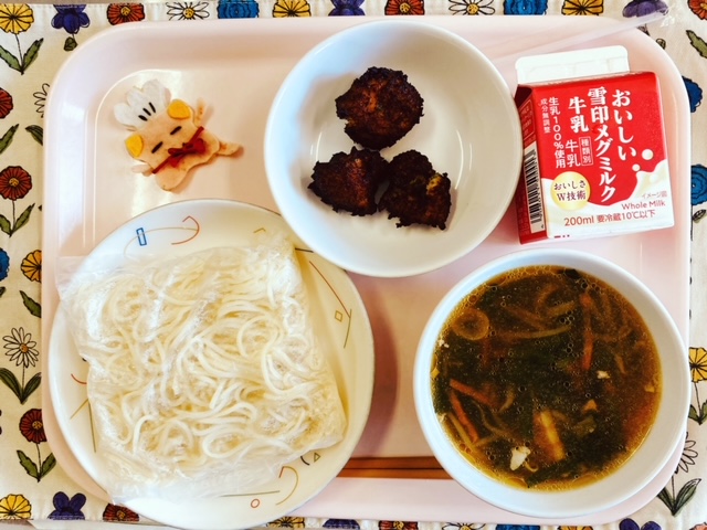 ピンクのトレーに給食が右上から反時計回りで牛乳、じゃがいものひとくちあげ、コック帽をかぶった布製マスコット、麺、しょうゆラーメンのスープと並べられている写真