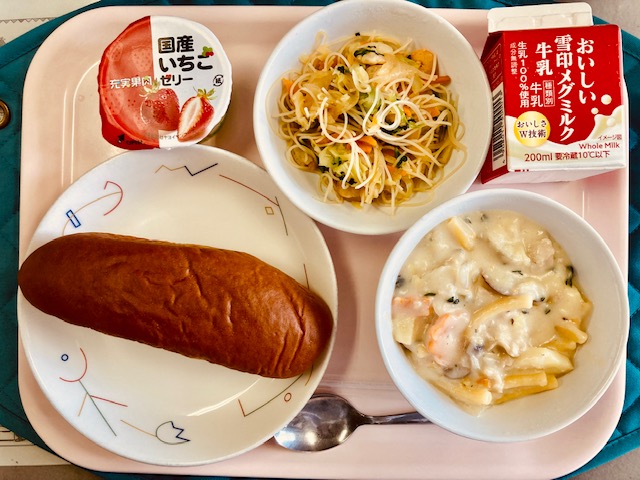 ピンクのトレーに給食が右上から反時計回りで牛乳、ビーフンソテー、国産いちごゼリー、くろパン、さつまいものクリーム煮と並べられている写真