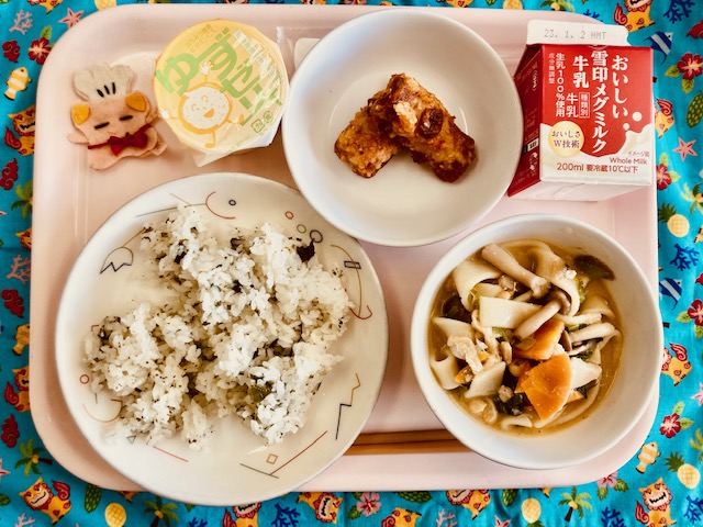 ピンクのトレーに給食が右上から反時計回りで牛乳、ちくわのころも揚げ、ゆずゼリー、コック帽をかぶった布製マスコット、わかめごはん、ほうとうと並べられている写真