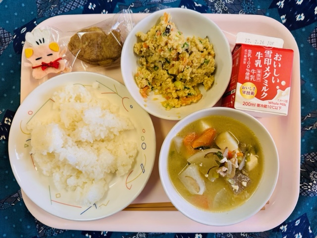 ピンクのトレーに給食が右上から反時計回りで牛乳、卯の花丼の具、ミニたい焼き、コック帽をかぶった布製マスコット、ごはん、トン汁と並んでいる写真