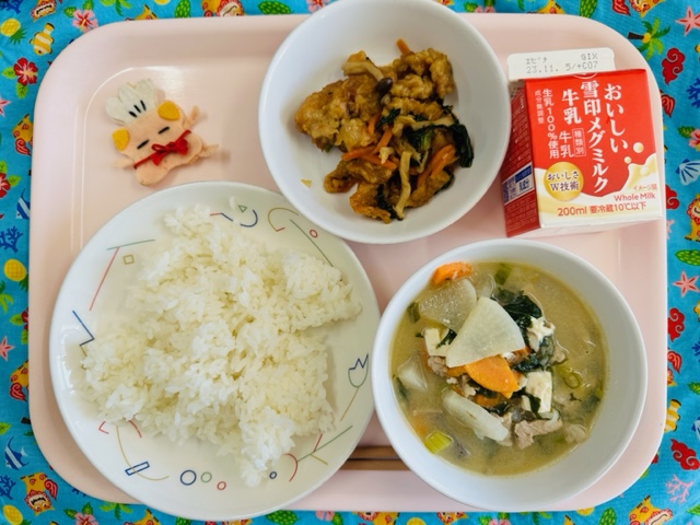 ピンクのトレーに給食が右上から反時計回りで牛乳、とりにくの香りあえ、コック帽をかぶった布製マスコット、ごはん、あっさりとんじると並べられている写真