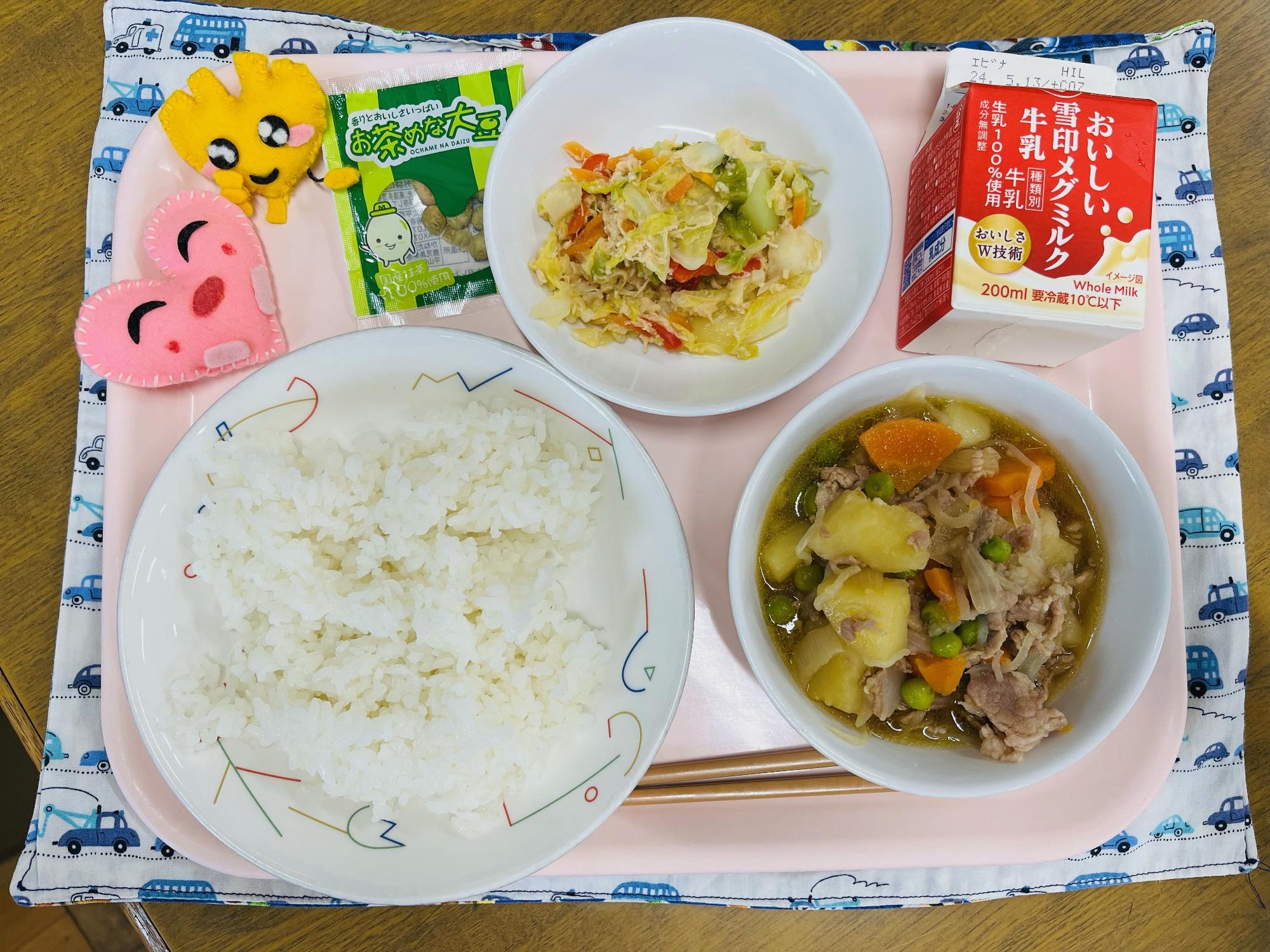 ピンクのトレーに給食が右上から反時計回りで牛乳、ささみとキャベツのサラダ、デザート、ハートの形をした黄色とピンク色の布製マスコット、ごはん、肉じゃがと並べられている写真