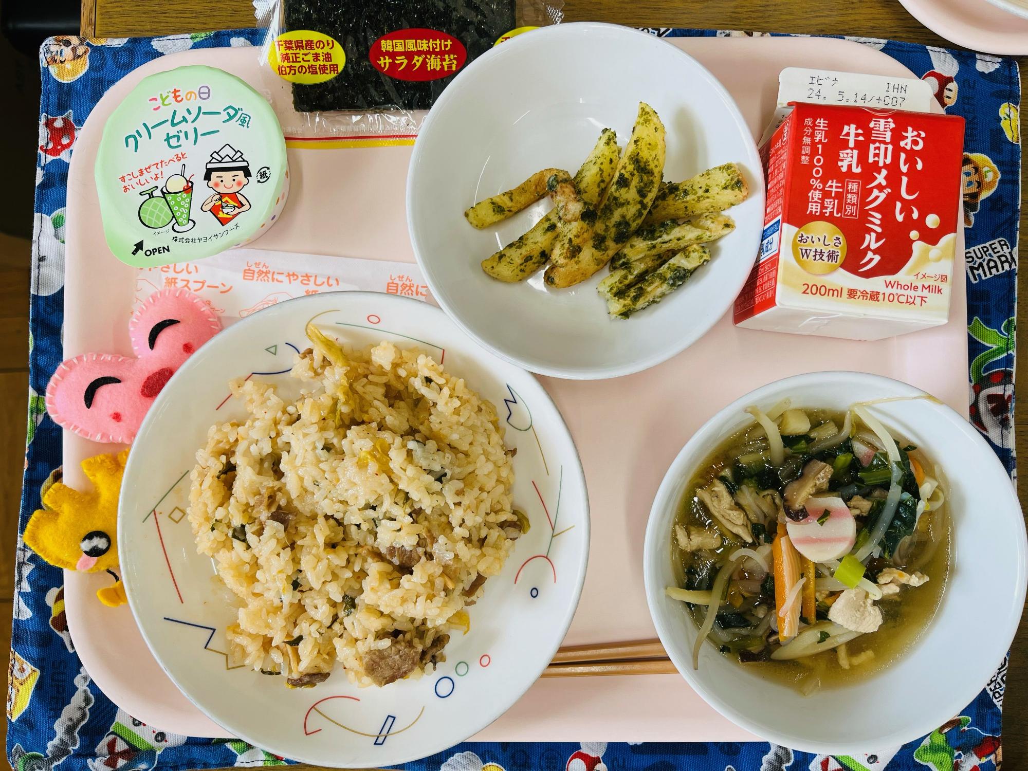 ピンクのトレーに給食が右上から反時計回りで牛乳、フライドポテト、サラダのり、デザート、ハートの形をした黄色とピンク色の布製マスコット、キムチごはん、五目スープと並べられている写真