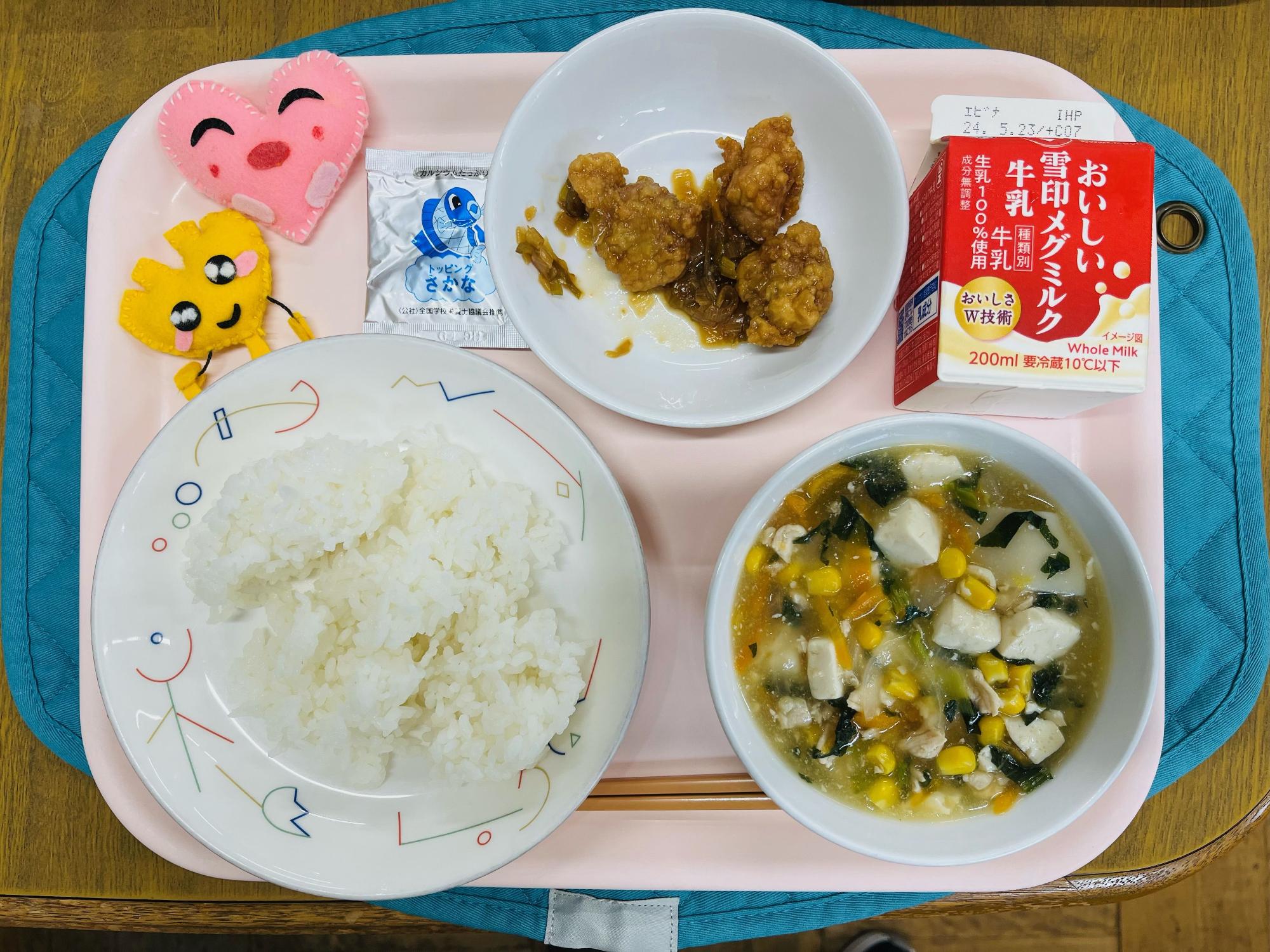 ピンクのトレーに給食が右上から反時計回りで牛乳、ユーリンチ、ふりかけ、ハートの形をした黄色とピンク色の布製マスコット、ごはん、ワンタンスープと並べられている写真