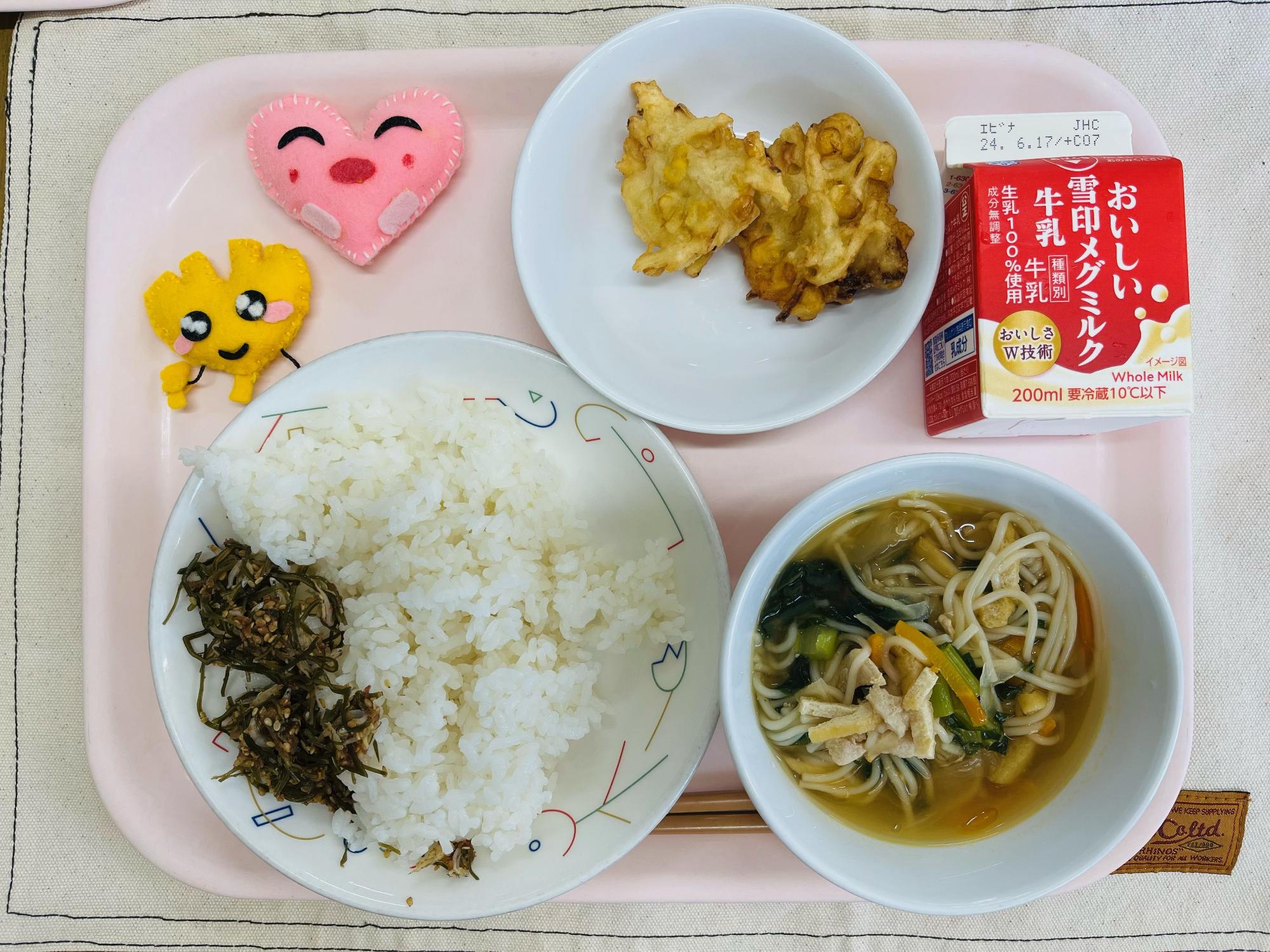 ピンクのトレーに給食が右上から反時計回りで牛乳、かきあげ、ハートの形をした黄色とピンク色の布製マスコット、ごはんとうめこんぶ、そうめん汁と並べられている写真