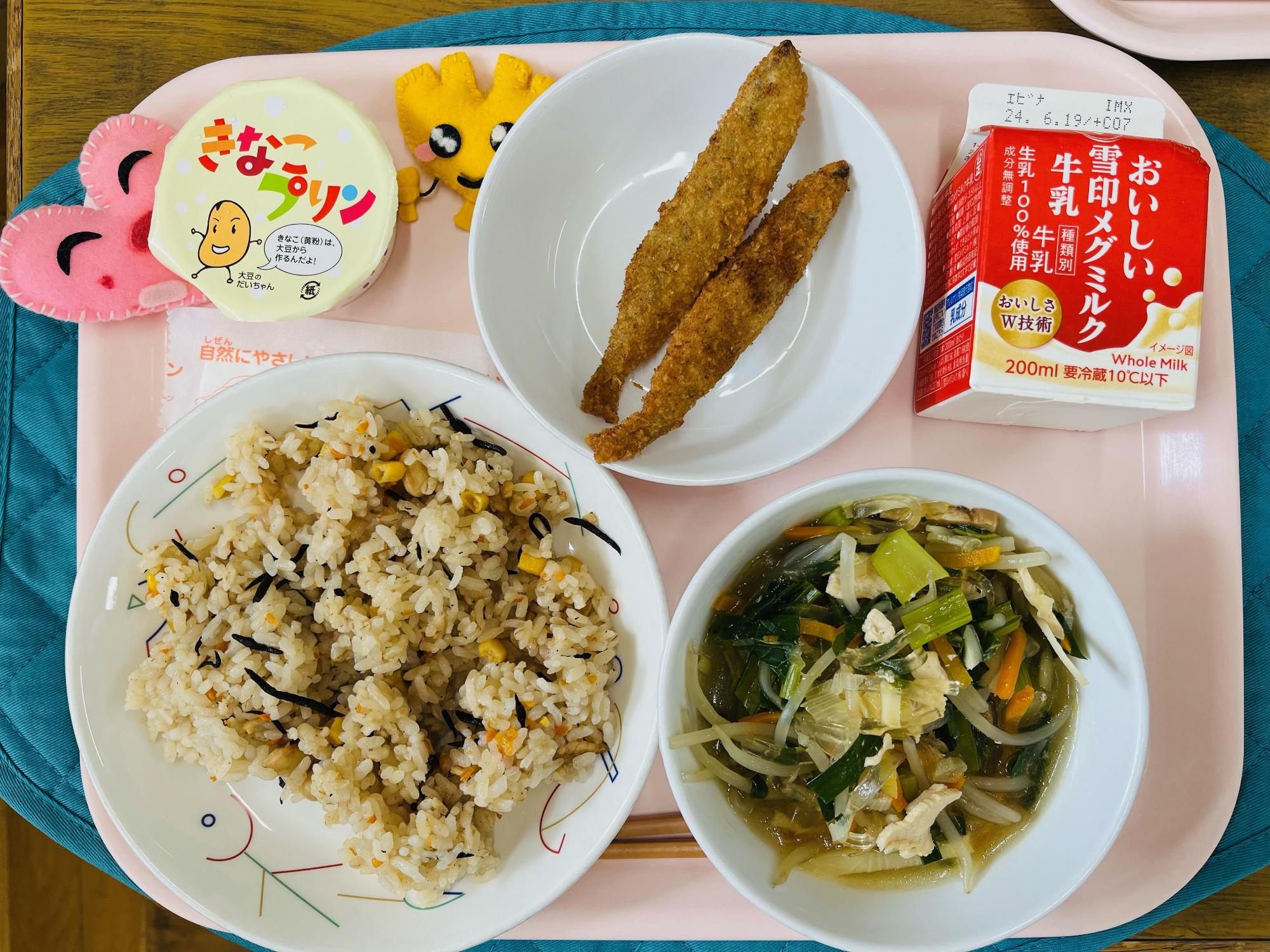 ピンクのトレーに給食が右上から反時計回りで牛乳、ししゃもフライ、きなこプリン、ハートの形をした黄色とピンク色の布製マスコット、かみかみライス、中華五目スープと並べられている写真