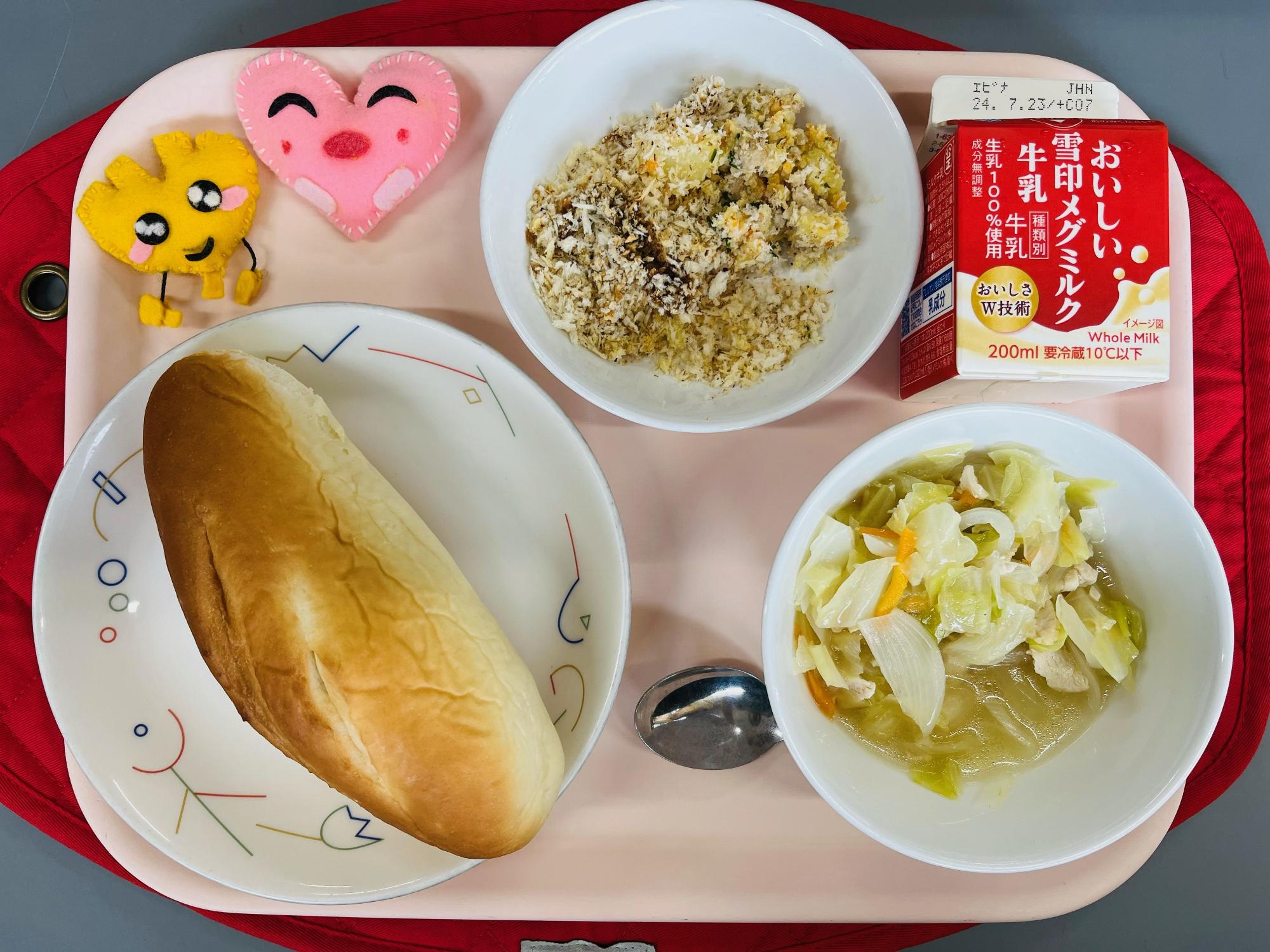 ピンクのトレーに給食が右上から反時計回りで牛乳、スコップコロッケ、ハートの形をした黄色とピンク色の布製マスコット、ミルクパン、キャベツのスープと並べられている写真