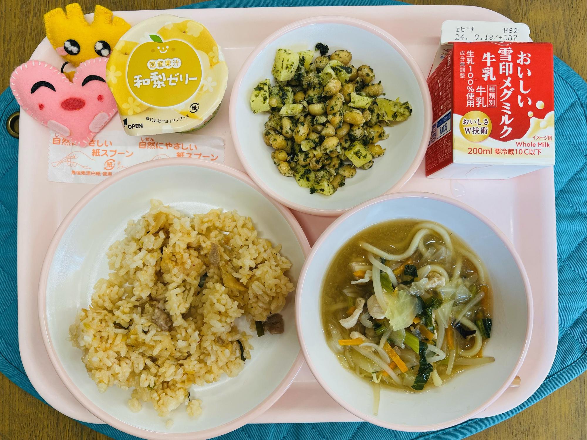 ピンクのトレーに給食が右上から反時計回りで牛乳、青のりポテトビーンズ、和梨ゼリー、ハートの形をした黄色とピンク色の布製マスコット、キムチご飯、ちゃんぽんスープと並べられている写真