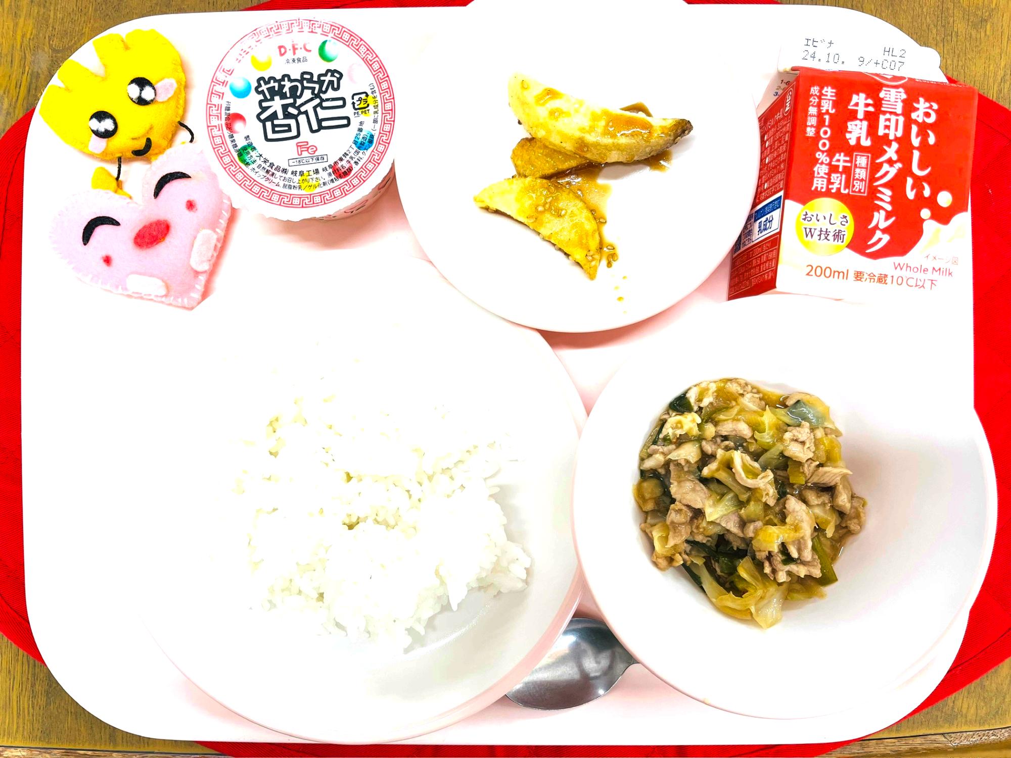ピンクのトレーに給食が右上から反時計回りで牛乳、じゃがいものゴマだれかけ、杏仁豆腐、ハートの形をした黄色とピンク色の布製マスコット、ごはん、ホイコーローと並べられている写真