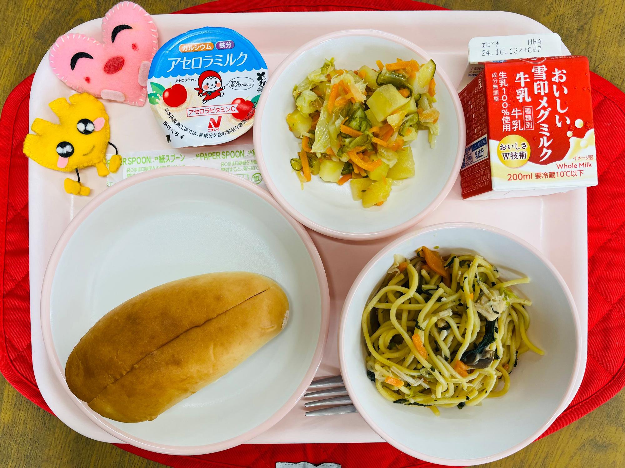 ピンクのトレーに給食が右上から反時計回りで牛乳、ポテトサラダ、アセロラミルクゼリー、ハートの形をした黄色とピンク色の布製マスコット、パン、和風スパゲッティと並べられている写真